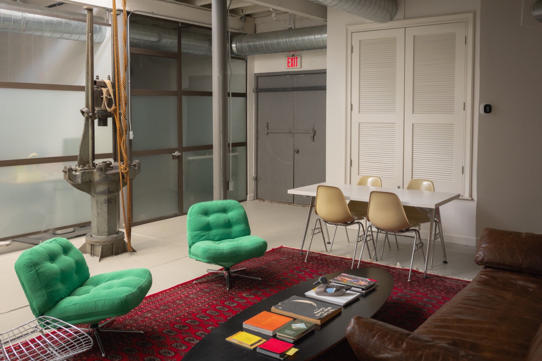The Ace Studio living room from the other side: green lounge chairs on a red rug, a long table and the building's original iron pulley.